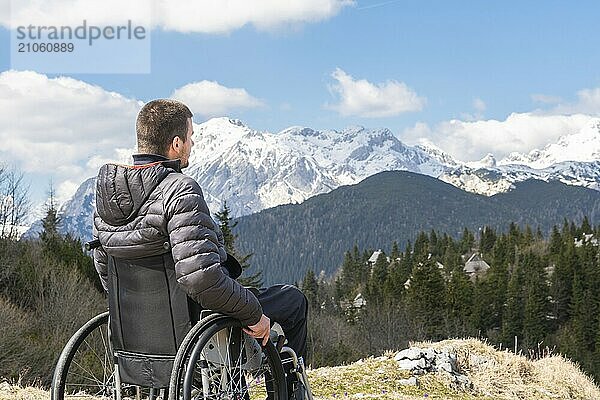 Foto eines jungen behinderten Mannes im Rollstuhl  der draußen in der Natur Berge und Natur beobachtet