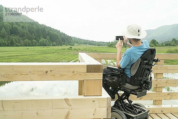 Mann im Rollstuhl mit Smartphone Kamera in der Nähe des Sees in der Natur