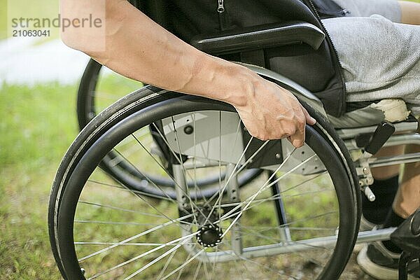 Junger behinderter Mann in einem Rollstuhl sitzend in der Natur  der die Räder dreht und hält