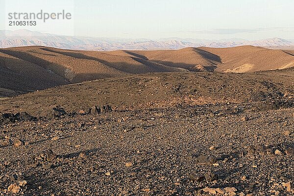 Atemberaubende Aussicht auf schwarze und rote felsige Berge mit einem Fluss auf dem Boden bei Sonnenuntergang in der Sahara Wüste in Marokko