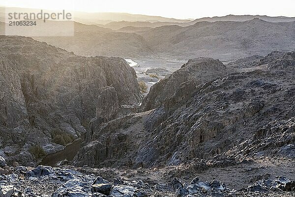 Atemberaubende Aussicht auf schwarze und rote felsige Berge mit einem Fluss auf dem Boden bei Sonnenuntergang in der Sahara Wüste in Marokko