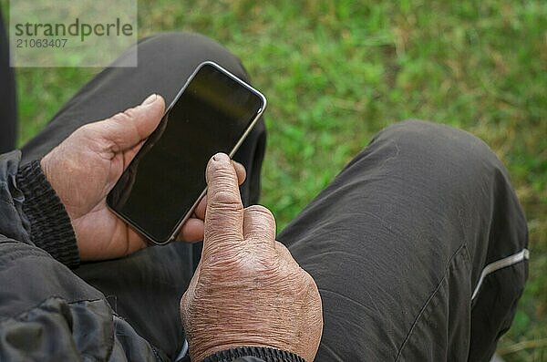 Nahaufnahme des faltigen Fingers eines Mannes  der ein Mobiltelefon berührt