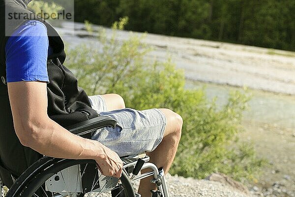 Glücklicher junger Mann im Rollstuhl draußen in der Natur an einem sonnigen Sommertag