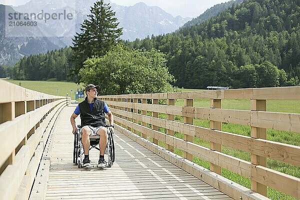 Behinderter junger Mann im Rollstuhl auf einem hölzernen Brückenpfad  der die Natur und die schöne Aussicht genießt