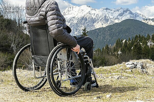 Junger behinderter Mann im Rollstuhl draußen in der Natur beim Beobachten von Bergen und Natur