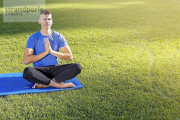 Junger Mann in Sportkleidung sitzt im Park und macht Yoga