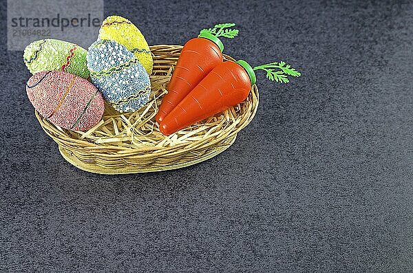 Ostern farbige Eier und Karotten in einem Korb vor einem trendigen schwarzen Hintergrund. Minimales Osterkonzept. Osterkarte mit Kopierraum für Text