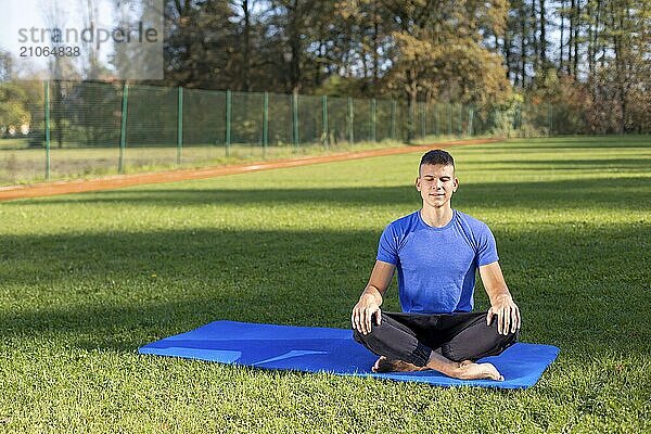 Junger Mann in Sportkleidung sitzt im Park und macht Yoga