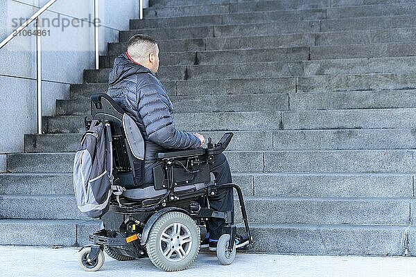 Junger behinderter Mann im Rollstuhl vor einer Treppe