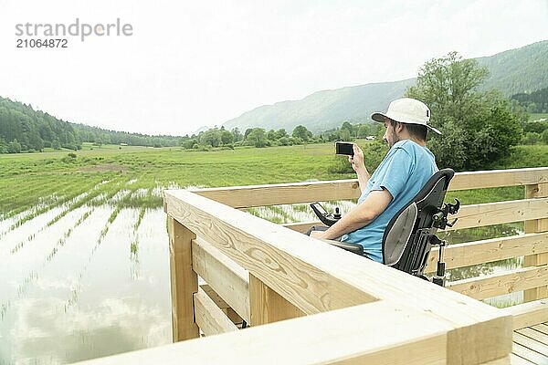 Mann im Rollstuhl mit Smartphone Kamera in der Nähe des Sees in der Natur