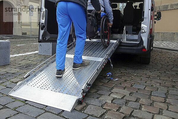 Assistent  der einer behinderten Person im Rollstuhl beim Transport über die Rampe eines zugänglichen Lieferwagens hilft