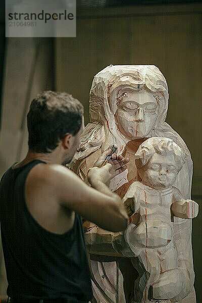 Ein Mann schnitzt in einer Werkstatt mit verschiedenen Werkzeugen eine Statue aus Holz