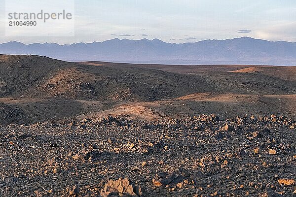 Atemberaubende Aussicht auf schwarze und rote felsige Berge mit einem Fluss auf dem Boden bei Sonnenuntergang in der Sahara Wüste in Marokko