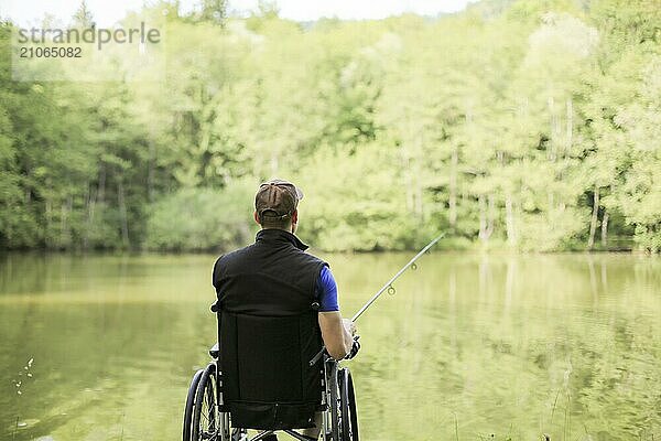 Fröhlicher und junger behinderter Mann beim Angeln an einem See in der Natur. Beliebter Sport für Querschnittsgelähmte