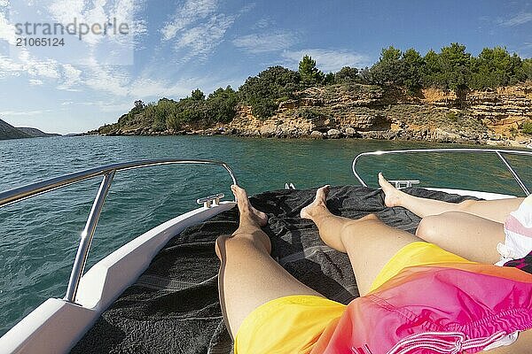 Blick auf Mann und Frau Beine liegen auf Yacht mit türkisblauem Meer und Strand mit grünen Palmen auf dem Hintergrund. Heterosexuelles Paar in Luxus Sommerurlaub Konzept