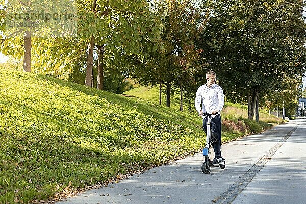 Fröhlicher und lässiger Mann fährt Elektroroller im Stadtpark