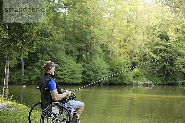 Fröhlicher und junger behinderter Mann beim Angeln an einem See in der Natur. Beliebter Sport für Querschnittsgelähmte