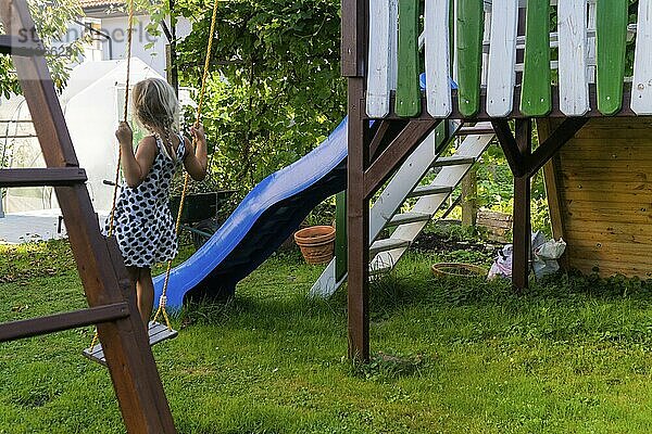 Kleines Kind blondes Mädchen mit Spaß auf einer Schaukel im Freien. Sommer Spielplatz. Mädchen schwingt hoch. Junges Kind auf Schaukel im Garten