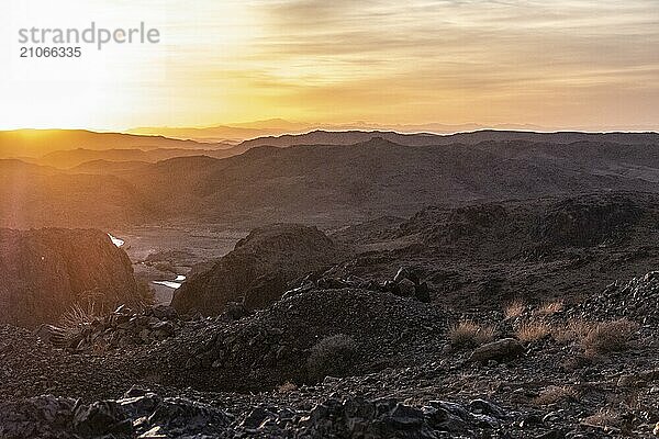 Atemberaubende Aussicht auf schwarze und rote felsige Berge mit einem Fluss auf dem Boden bei Sonnenuntergang in der Sahara Wüste in Marokko