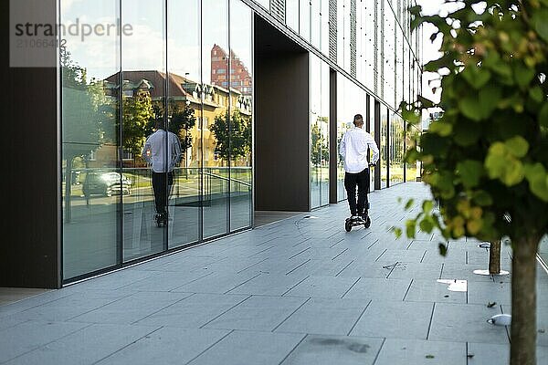 Junger und lässiger Geschäftsmann fährt Elektroroller in der Stadt