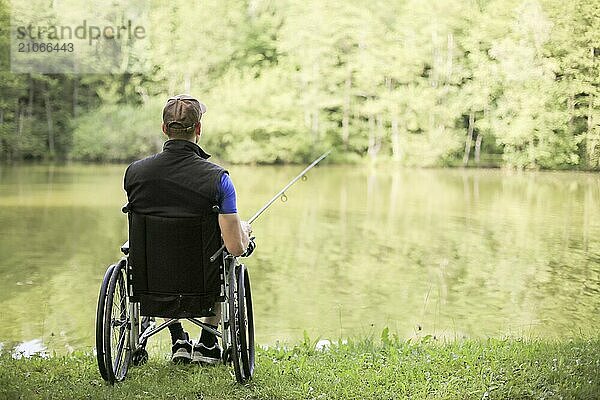 Fröhlicher und junger behinderter Mann beim Angeln an einem See in der Natur. Beliebter Sport für Querschnittsgelähmte