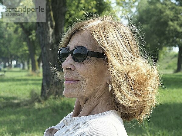 Glückliche ältere Frau mit stilvoller Sonnenbrille genießt einen sonnigen Tag im Park und strahlt Ruhe und Zuversicht aus