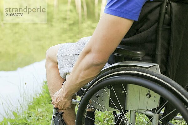 Junger behinderter Mann in einem Rollstuhl sitzend in der Natur  der die Räder dreht und hält