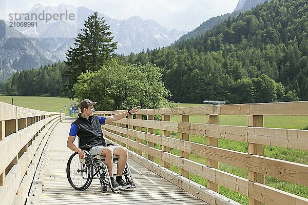 Behinderter junger Mann im Rollstuhl auf einem hölzernen Brückenpfad  der die Natur und die schöne Aussicht genießt