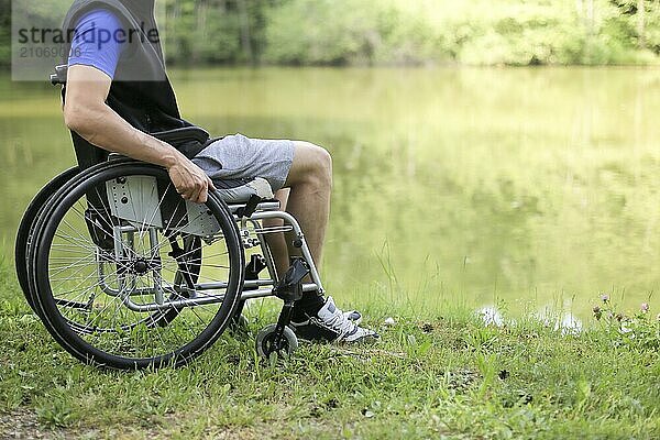 Glücklicher junger behinderter Mann in einem Rollstuhl sitzend in der Natur