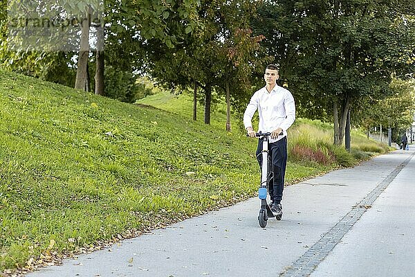 Fröhlicher und lässiger Mann fährt Elektroroller im Stadtpark