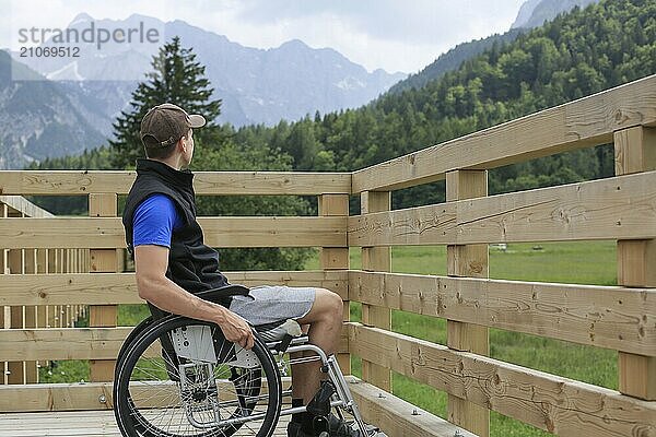 Behinderter junger Mann im Rollstuhl auf einem hölzernen Brückenpfad  der die Natur und die schöne Aussicht genießt