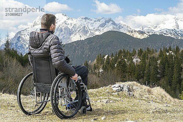 Foto eines jungen behinderten Mannes im Rollstuhl  der draußen in der Natur Berge und Natur beobachtet