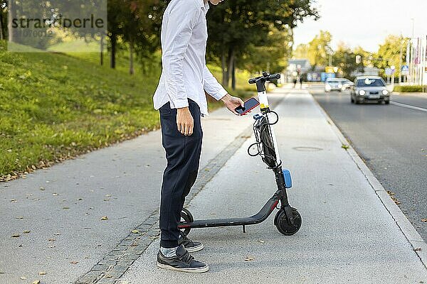 Lässiger Mann  der eine Smartphone App benutzt und einen Elektroroller zum Mieten in der Stadt freischaltet