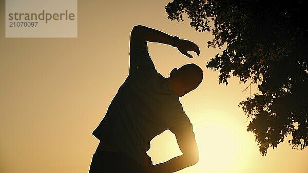 Ein Mann wärmt sich mit einer Beinstreckübung vor einem intensiven Training im Freien bei Sonnenuntergang auf. Gesunder und aktiver Lebensstil