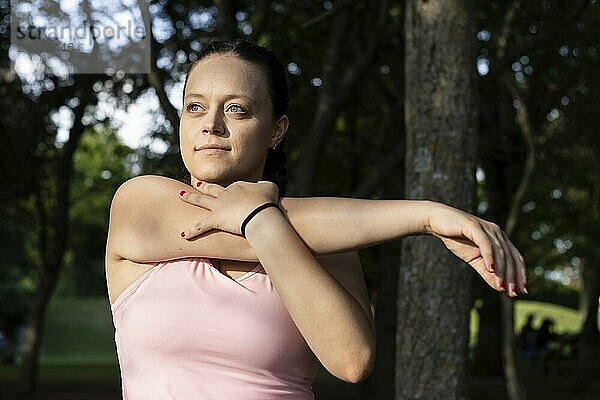 Vorderansicht einer selbstbewussten jungen Frau  die ihre Arme dehnt  bevor sie im Park trainiert