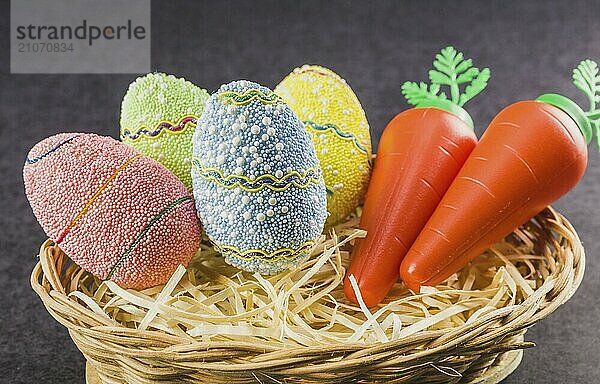 Ostern farbige Eier und Karotten in einem Korb vor einem trendigen schwarzen Hintergrund. Minimales Osterkonzept. Osterkarte mit Kopierraum für Text