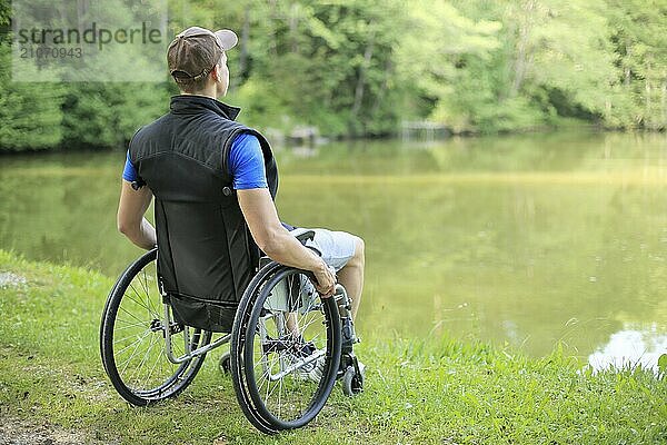 Glücklicher und junger behinderter Mann im Rollstuhl sitzend mit Blick auf einen schönen See in der Natur