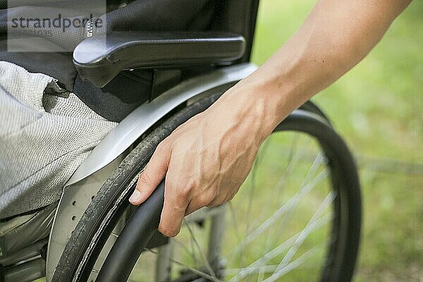 Junger behinderter Mann in einem Rollstuhl sitzend in der Natur  der die Räder dreht und hält