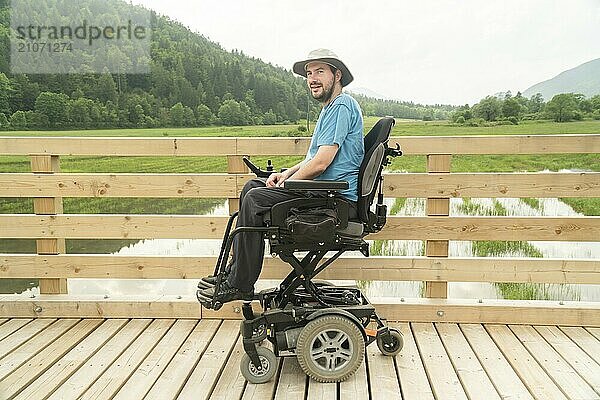 Foto eines behinderten jungen Mannes im elektrischen Rollstuhl auf einer Promenade  der seine Freiheit genießt und die Natur beobachtet