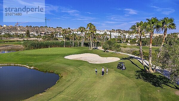 Luftaufnahme eines Golfplatzes mit Menschen darauf  die neben einem Wagen Golf spielen