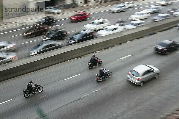 Schwenk von Motorrädern mit hoher Geschwindigkeit auf einer Allee in der Innenstadt von einem nahe gelegenen Gebäude mit langsameren Autos auf der Gegenfahrbahn. Keine Menschen