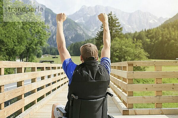 Behinderter junger Mann im Rollstuhl in der Natur  aufgeregt und voller Optimismus wie ein Gewinner