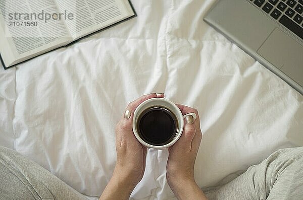 Frau mit gekreuzten Beinen  die ein Buch liest und Kaffee trinkt  Computer im Bett. Von oben gesehen