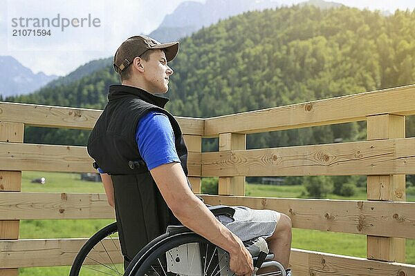 Behinderter junger Mann im Rollstuhl auf einem hölzernen Brückenpfad  der die Natur und die schöne Aussicht genießt