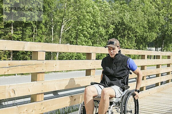 Behinderter junger Mann im Rollstuhl auf einem Holzbrückenweg in der Natur