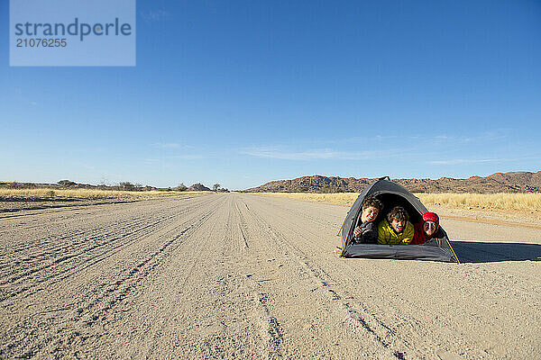 Three people lying in small tent pitched in middle of dirt road across savannah  Erongo Region  Namibia