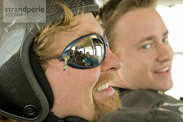 A skydive instructor and student sit in the belly of the plane waiting to exit and begin skydiving.