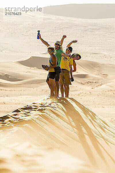 Group of friends standing in Namib Desert smiling and waving while looking at camera  Namibia