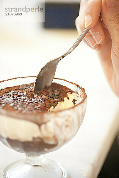 A customer samples freshly made tiramisu from a glass desert bowl.