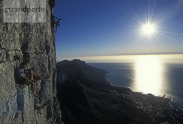 Two men rock climb on cliffs above the Atlantic Ocean  Cape Town  South Africa.